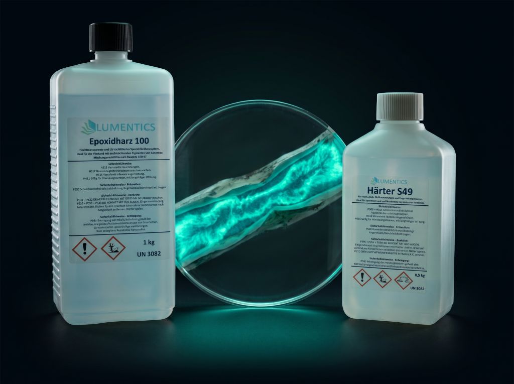Clear cast resin disc with an embedded aqua glowing vein in front of two resin bottles
