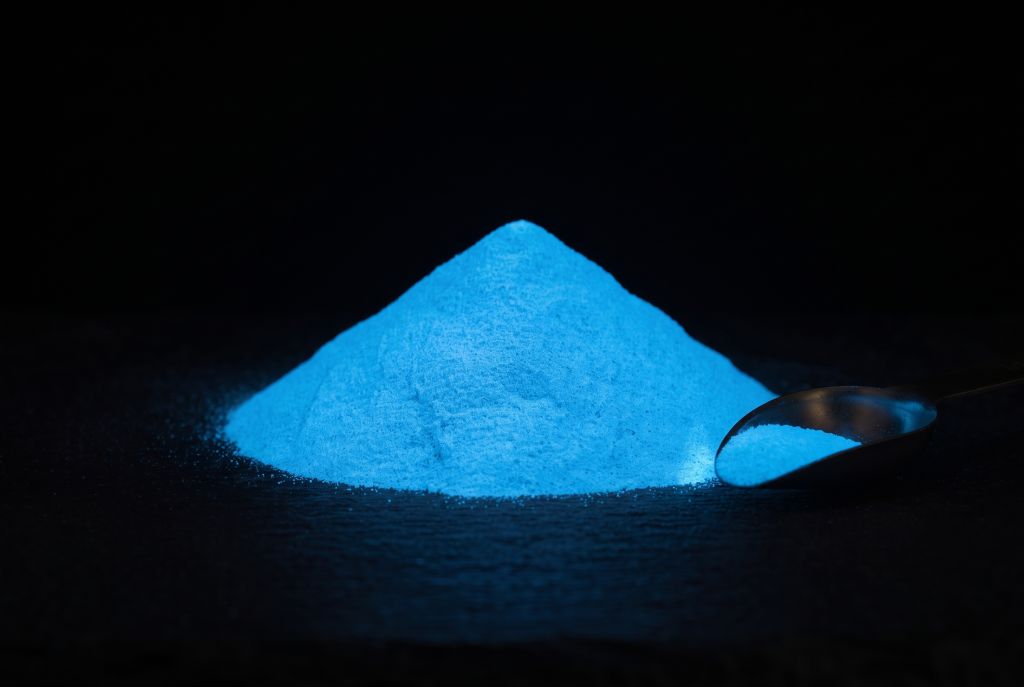 Photoluminescent pigment, blue, as a heap with a scoop, glowing in the dark