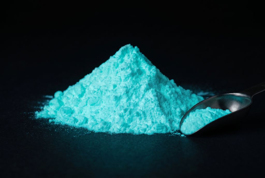 Photoluminescent pigment, blue-green, as a heap with a scoop, glowing in the dark