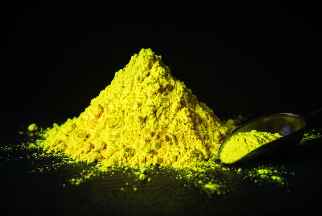 Nachleuchtpigment Gelb-Neongelb als Häufchen mit Messlöffel im Dunkeln leuchtend