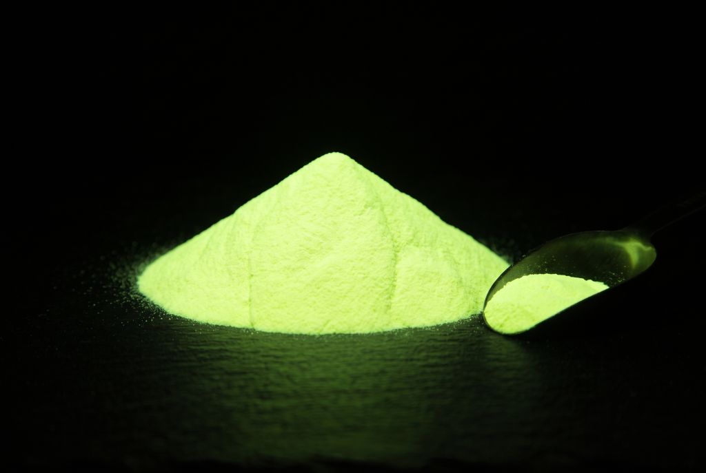 Photoluminescent pigment, yellow-green, as a heap with a scoop, glowing in the dark