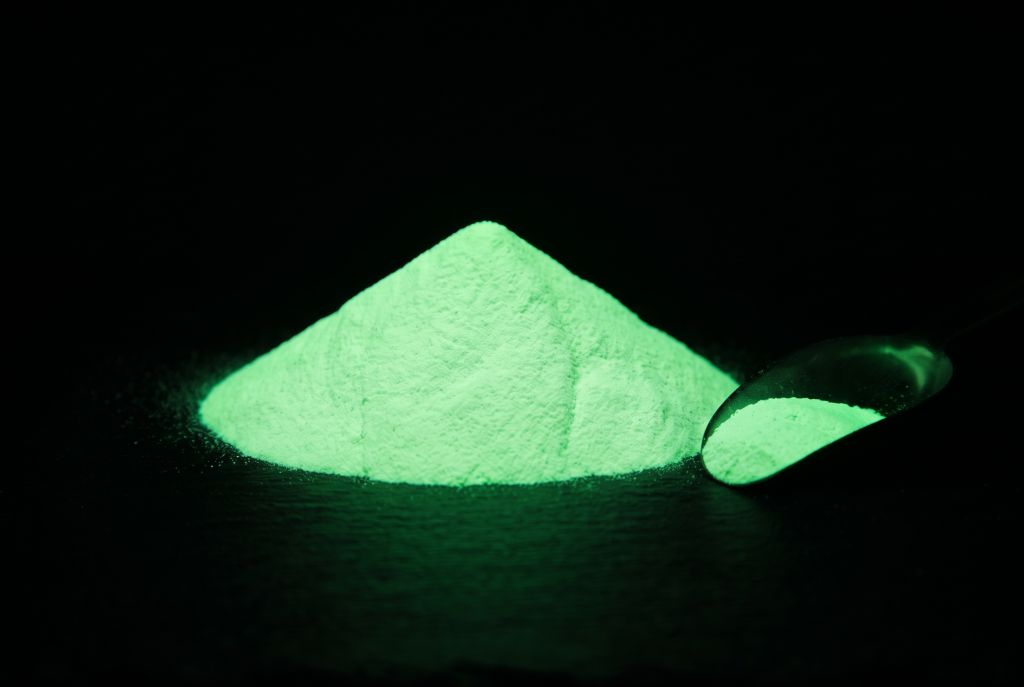 Nachleuchtpigment Natur-Grün als Häufchen mit Messlöffel, im Dunkeln grün leuchtend