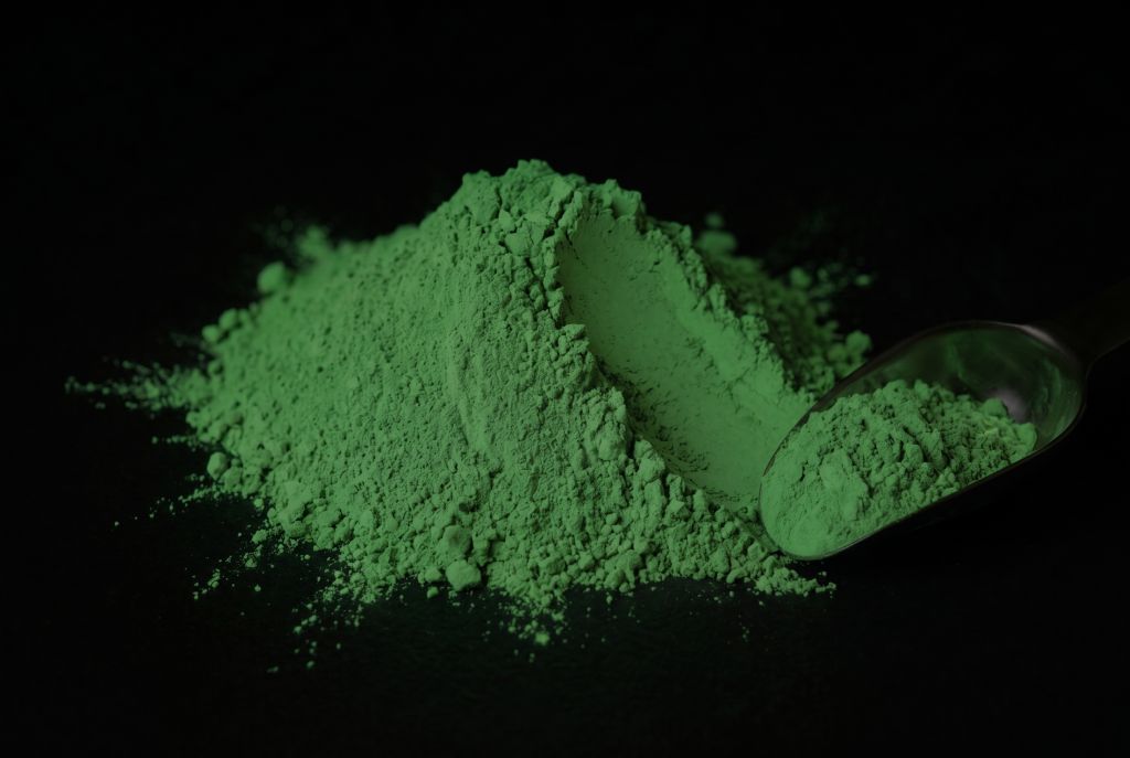 Nachleuchtpigment Grün-Grün als Häufchen mit Messlöffel im Dunkeln leuchtend