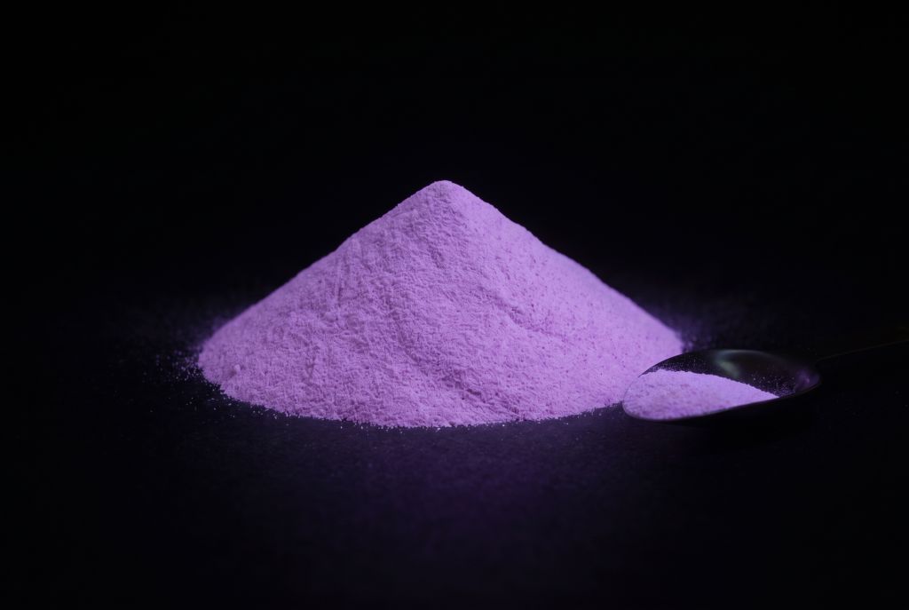 Photoluminescent pigment, violet, as a heap with a scoop, glowing in the dark