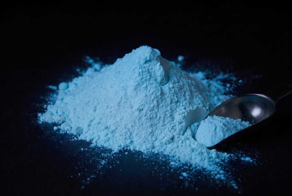 Nachleuchtpigment Natur-Blau als Häufchen mit Messlöffel im Dunkeln leuchtend