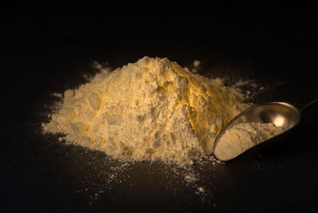Nachleuchtpigment Natur-Gelb als Häufchen mit Messlöffel im Dunkeln leuchtend
