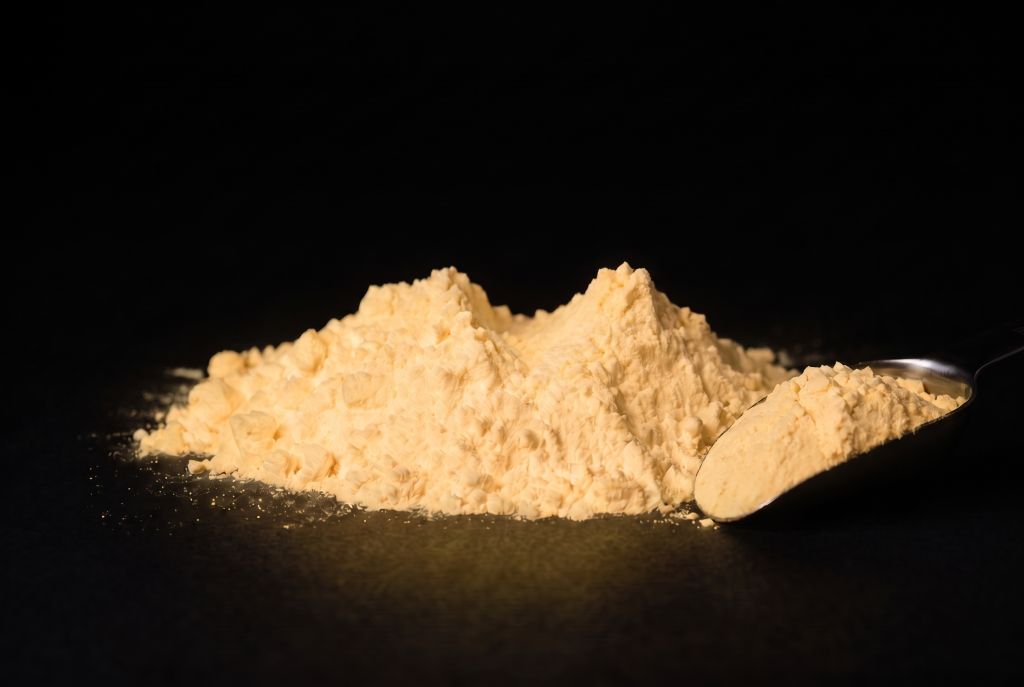 Nachleuchtpigment Natur-Orange als Häufchen mit Messlöffel im Dunkeln leuchtend