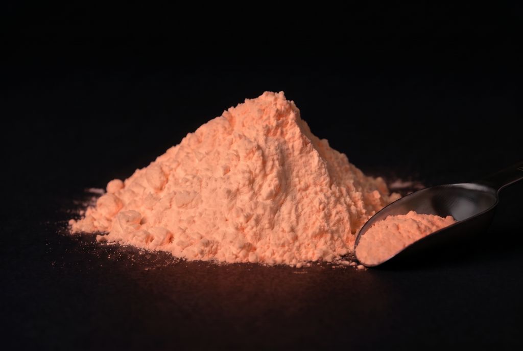 Nachleuchtpigment Natur-Orangerot als Häufchen mit Messlöffel im Dunkeln leuchtend