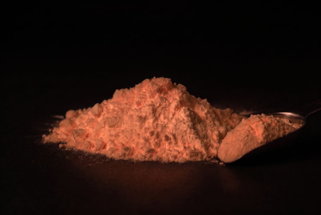 Nachleuchtpigment Natur-Rot als Häufchen mit Messlöffel im Dunkeln leuchtend