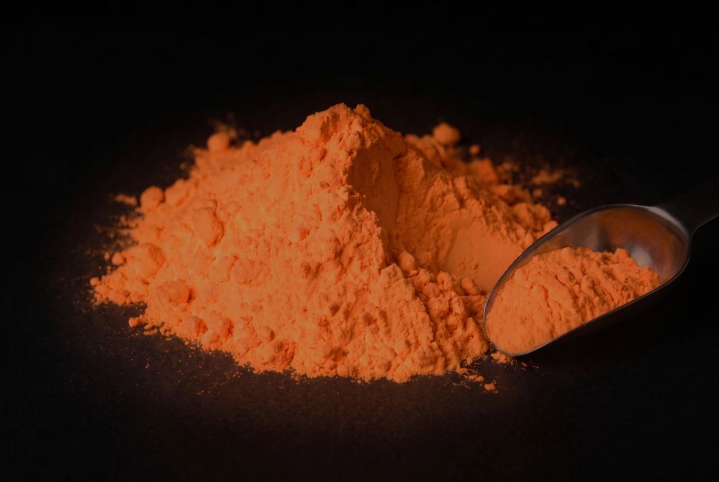 Nachleuchtpigment Orange als Häufchen mit Messlöffel im Dunkeln leuchtend