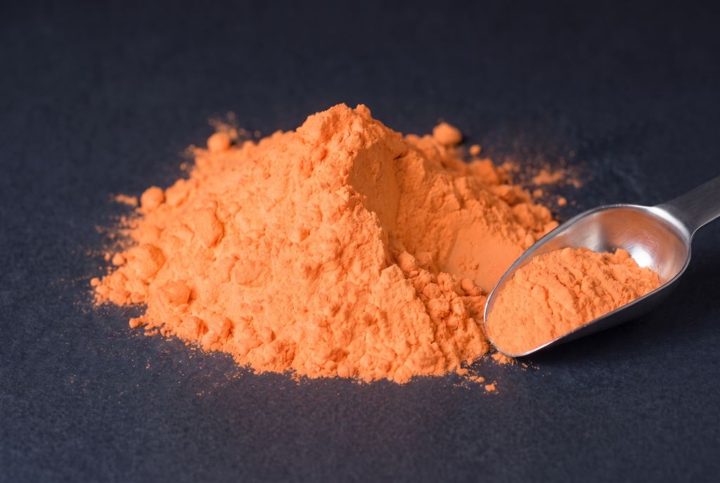 Nachleuchtpigment Orange als Häufchen mit Messlöffel bei Tageslicht