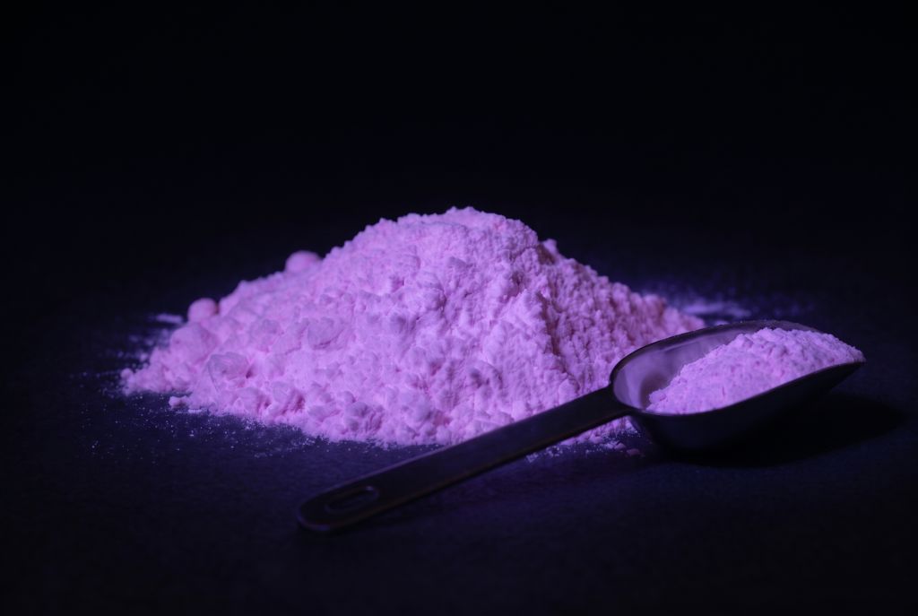 Nachleuchtpigment Pink-Lila als Häufchen mit Messlöffel im Dunkeln leuchtend