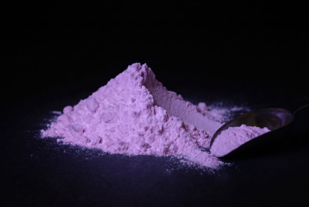 Nachleuchtpigment Pink-Oceanpink als Häufchen mit Messlöffel im Dunkeln leuchtend