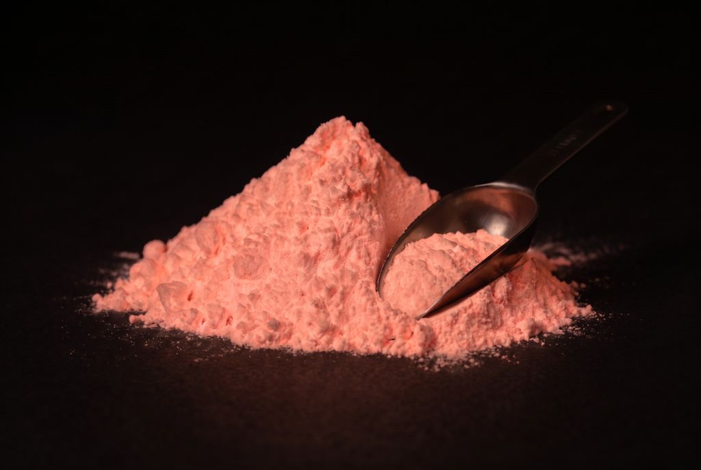 Nachleuchtpigment Pink-Pink als Häufchen mit Messlöffel im Dunkeln leuchtend