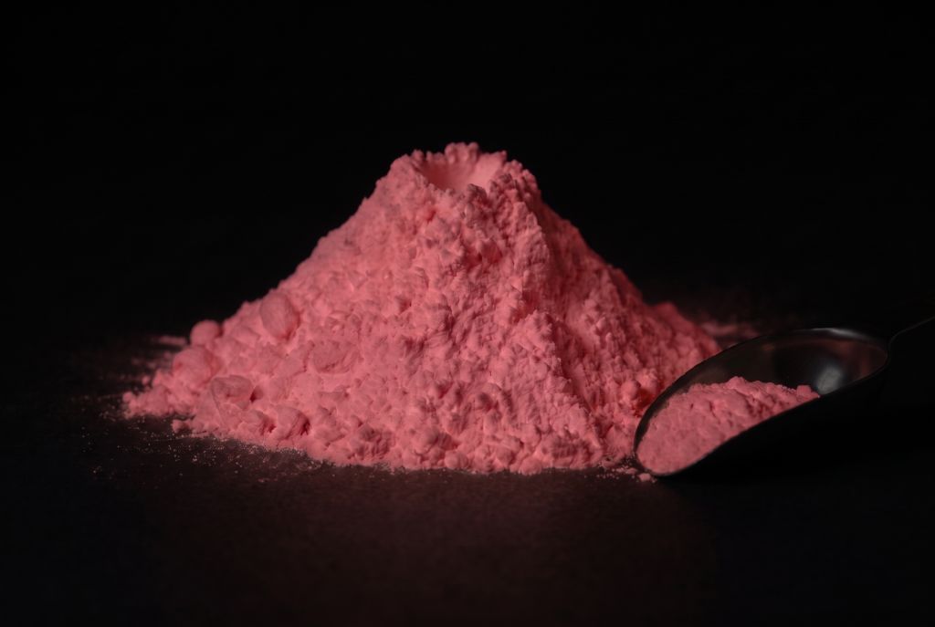 Nachleuchtpigment Pink-Rosarot als Häufchen mit Messlöffel im Dunkeln leuchtend