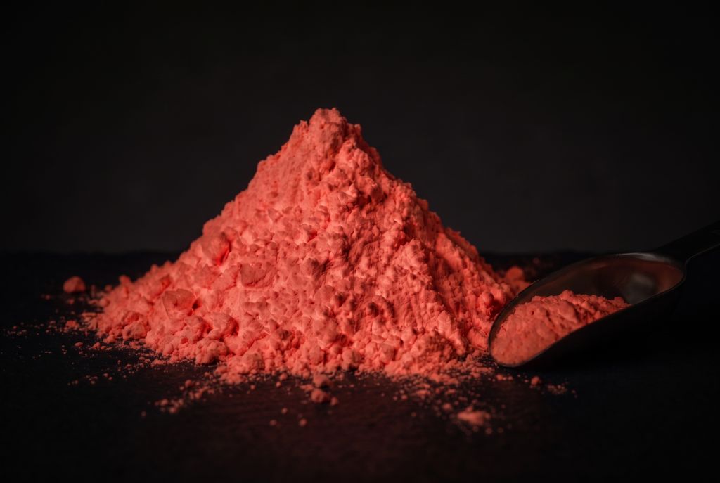 Nachleuchtpigment Rot als Häufchen mit Messlöffel im Dunkeln leuchtend