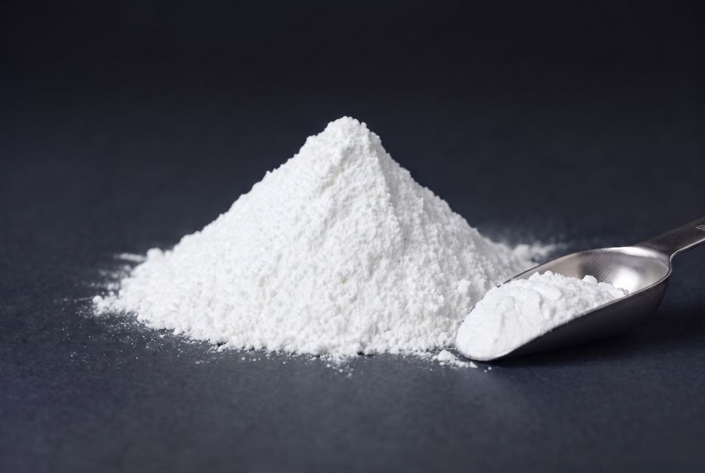 Nachleuchtpigment mit weißem Tagesfarbton als Häufchen mit Messlöffel bei Tageslicht